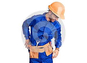 Young hispanic man wearing worker uniform suffering of backache, touching back with hand, muscular pain