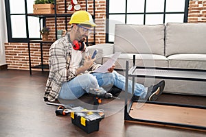 Young hispanic man worker reading instructions holding screwdriver at home