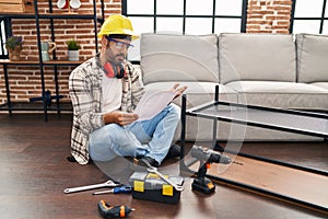 Young hispanic man worker reading instructions holding wrench at home