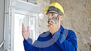 Young hispanic man worker talking on walkie-talkie at construction site