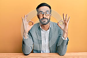 Young hispanic man working at the office relax and smiling with eyes closed doing meditation gesture with fingers