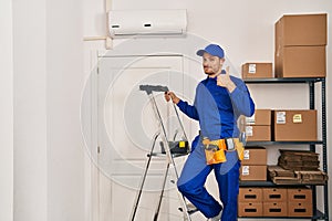 Young hispanic man working at renovation smiling happy and positive, thumb up doing excellent and approval sign