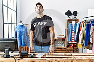 Young hispanic man working at retail boutique making fish face with lips, crazy and comical gesture