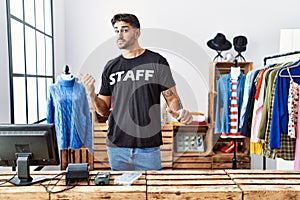 Young hispanic man working at retail boutique pointing to the back behind with hand and thumbs up, smiling confident