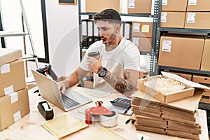 Young hispanic man working at small business ecommerce with laptop afraid and shocked with surprise and amazed expression, fear