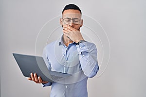 Young hispanic man working using computer laptop bored yawning tired covering mouth with hand