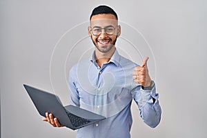 Young hispanic man working using computer laptop doing happy thumbs up gesture with hand