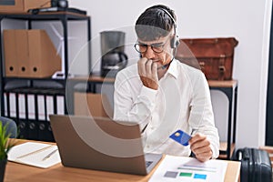 Young hispanic man working using computer laptop holding credit card looking stressed and nervous with hands on mouth biting nails