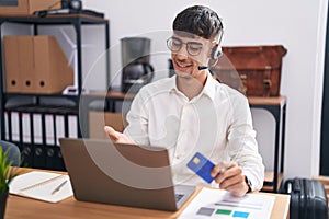 Young hispanic man working using computer laptop holding credit card smiling cheerful offering palm hand giving assistance and
