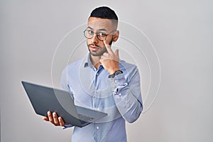 Young hispanic man working using computer laptop pointing to the eye watching you gesture, suspicious expression