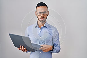 Young hispanic man working using computer laptop skeptic and nervous, frowning upset because of problem