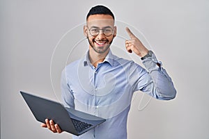 Young hispanic man working using computer laptop smiling amazed and surprised and pointing up with fingers and raised arms