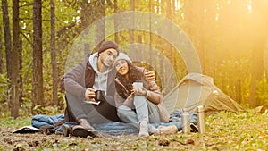 Young hispanic married couple tourists rest in woods camping man and woman in love drinking hot tea talking cute loving