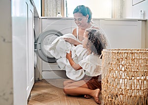 Young hispanic mother and her daughter sorting dirty laundry in the washing machine at home. Adorable little girl and