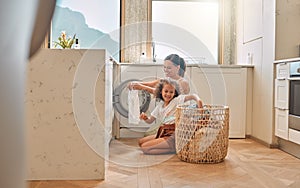 Young hispanic mother and her daughter sorting dirty laundry in the washing machine at home. Adorable little girl and