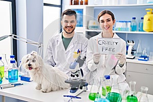 Young hispanic people working at scientist laboratory with dog smiling with a happy and cool smile on face