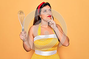 Young hispanic pin up woman wearing fashion sexy 50s style holding cooking whisk blender serious face thinking about question,