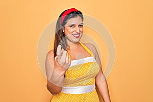 Young hispanic pin up woman wearing fashion sexy 50s style over yellow background Beckoning come here gesture with hand inviting