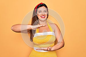 Young hispanic pin up woman wearing fashion sexy 50s style over yellow background gesturing with hands showing big and large size