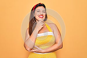 Young hispanic pin up woman wearing fashion sexy 50s style over yellow background looking confident at the camera smiling with