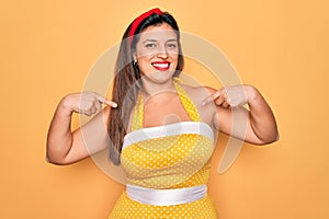 Young hispanic pin up woman wearing fashion sexy 50s style over yellow background looking confident with smile on face, pointing