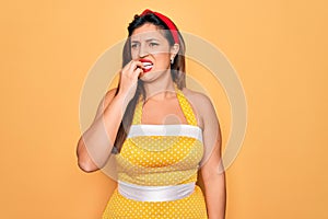 Young hispanic pin up woman wearing fashion sexy 50s style over yellow background looking stressed and nervous with hands on mouth