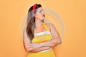 Young hispanic pin up woman wearing fashion sexy 50s style over yellow background looking to the side with arms crossed convinced