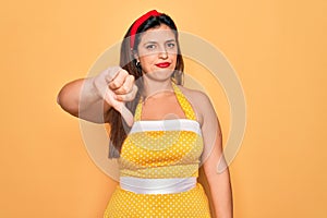 Young hispanic pin up woman wearing fashion sexy 50s style over yellow background looking unhappy and angry showing rejection and