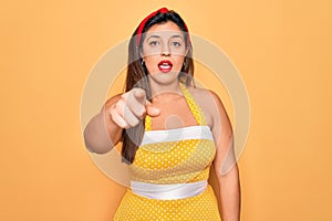 Young hispanic pin up woman wearing fashion sexy 50s style over yellow background pointing displeased and frustrated to the