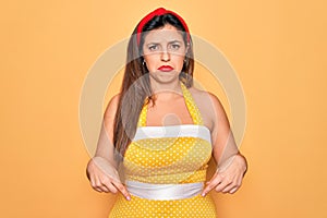 Young hispanic pin up woman wearing fashion sexy 50s style over yellow background Pointing down looking sad and upset, indicating