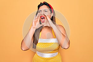 Young hispanic pin up woman wearing fashion sexy 50s style over yellow background Shouting angry out loud with hands over mouth