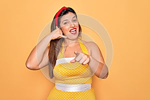 Young hispanic pin up woman wearing fashion sexy 50s style over yellow background smiling doing talking on the telephone gesture