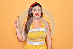 Young hispanic pin up woman wearing fashion sexy 50s style over yellow background smiling looking to the camera showing fingers