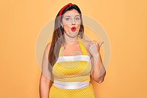 Young hispanic pin up woman wearing fashion sexy 50s style over yellow background Surprised pointing with hand finger to the side,