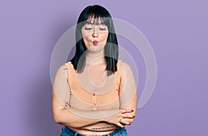 Young hispanic plus size woman with arms crossed gesture making fish face with mouth and squinting eyes, crazy and comical