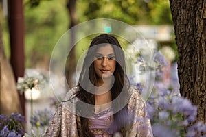 Young, Hispanic, pretty, brunette woman in an elegant vintage violet dress, seen through violet flowers. Concept of beauty,