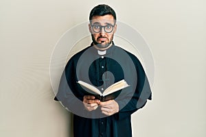 Young hispanic priest man holding bible depressed and worry for distress, crying angry and afraid