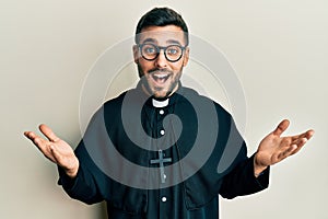 Young hispanic priest man standing over white background smiling and laughing hard out loud because funny crazy joke