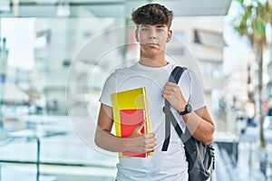 Young hispanic teenager student smiling confident holding books at university