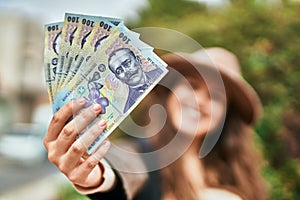 Young hispanic tourist woman smiling happy holding romania lei banknotes at the city