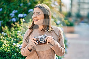 Young hispanic tourist woman smiling happy using vintage camera at the city