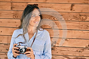 Young hispanic tourist woman smiling happy using vintage camera at the city