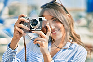 Young hispanic tourist woman smiling happy using vintage camera at the port