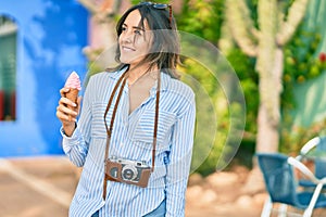 Young hispanic tourist woman using vintage camera and eating ice cream at the port
