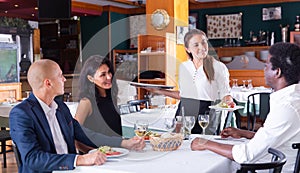 Young hispanic waitress serving meals to company in restaurant