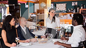 Young hispanic waitress serving meals to company in restaurant