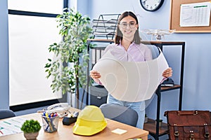 Young hispanic woman architect reading blueprints at office