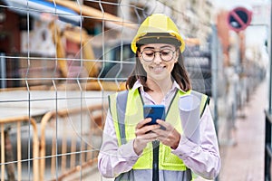 Young hispanic woman architect using smartphone holding blueprints at street