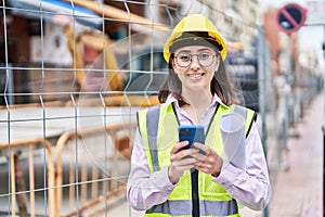 Young hispanic woman architect using smartphone holding blueprints at street