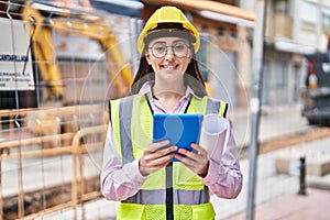 Young hispanic woman architect using touchpad holding blueprints at street